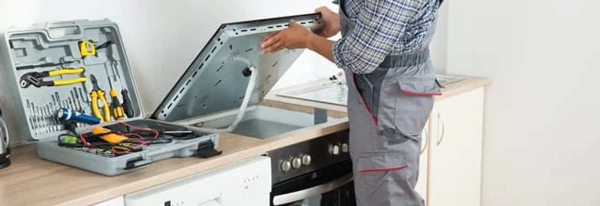 Cooktop repair technician lifting a built-in stovetop for service in Gilbert, AZ